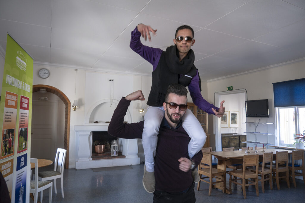 Adullah står med Khalid på sina axlar i en lokal och båda gestikulerar med armarna.