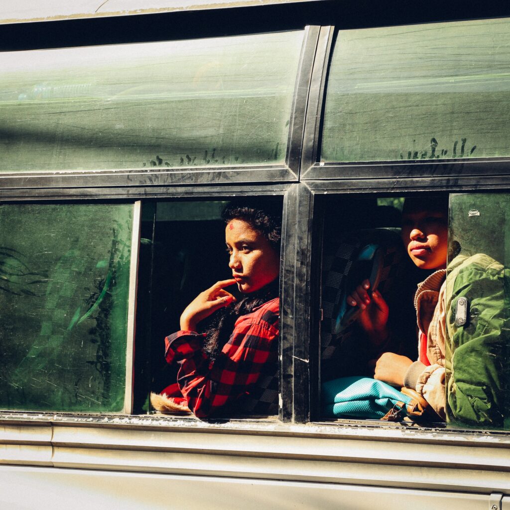 Två personer sitter i en buss och tittar ut genom varsitt fönster. En av dem har ett rött, nepalesiskt bindimärke i pannan.